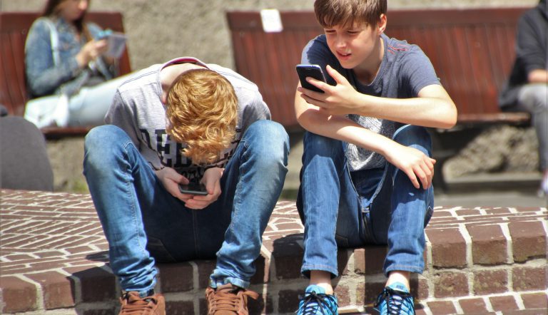 Twee pubers op een stoepje, starend naar een beeldscherm